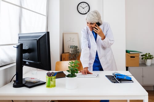 Clinician standing at computer on the phone with a patient reviewing medical history in an EHR system.