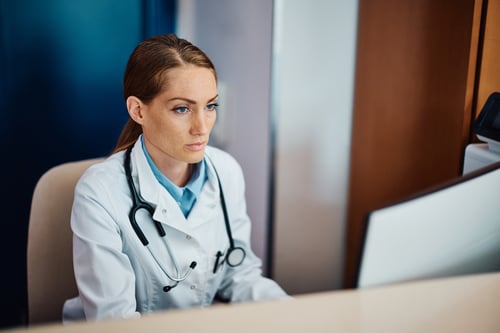 A doctor sits at a desk working on a desktop computer