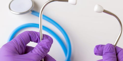 Stethoscope being held by hands wearing purple gloves