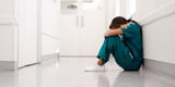 Nurse suffering from burnout sitting in hallway with head down 