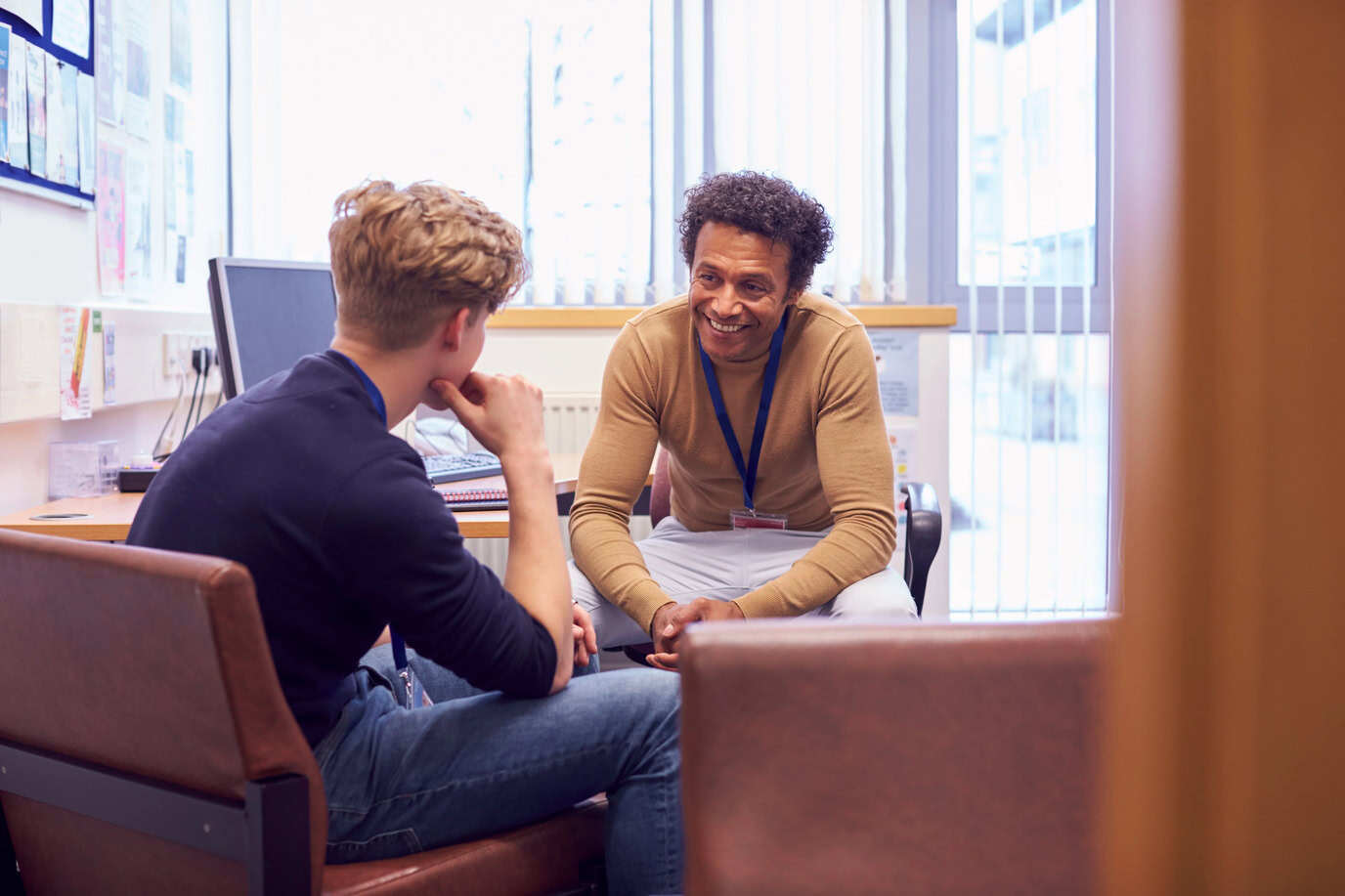 A behavioral health counselor in a warm one-on-one session with a young adult patient, engaged in an attentive and supportive conversation in a clinical office setting