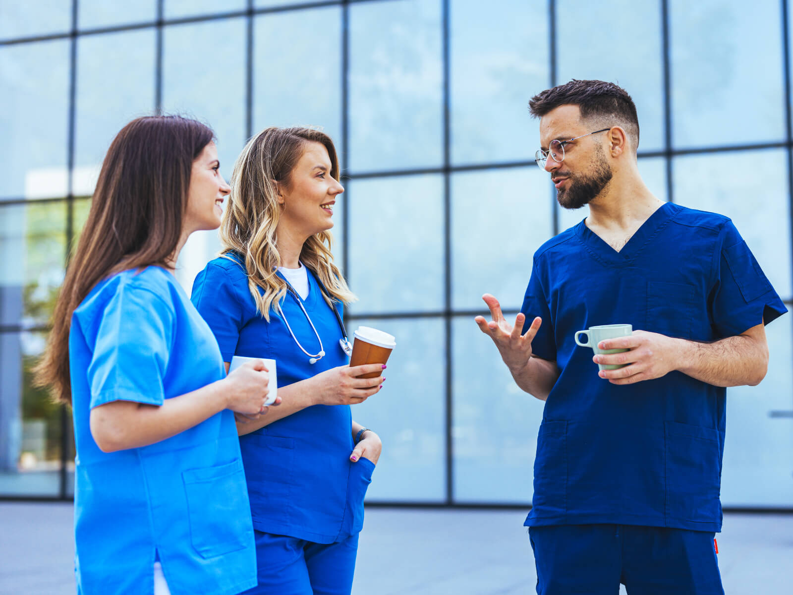 Healthcare professionals in blue scrubs having a conversation outside a medical facility.